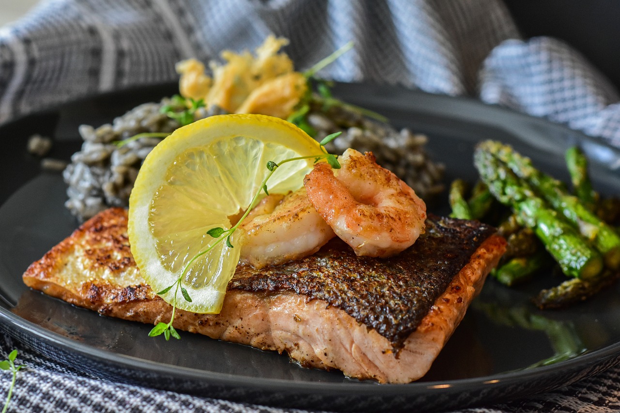 A plate of salmon and shrimp assembled with a lemon wedge atop it.