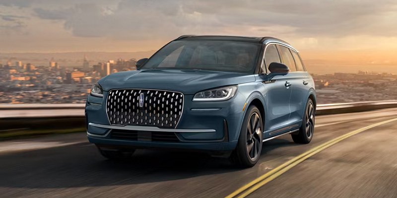 Blue Lincoln SUV driving on a highway with a city skyline in the background.