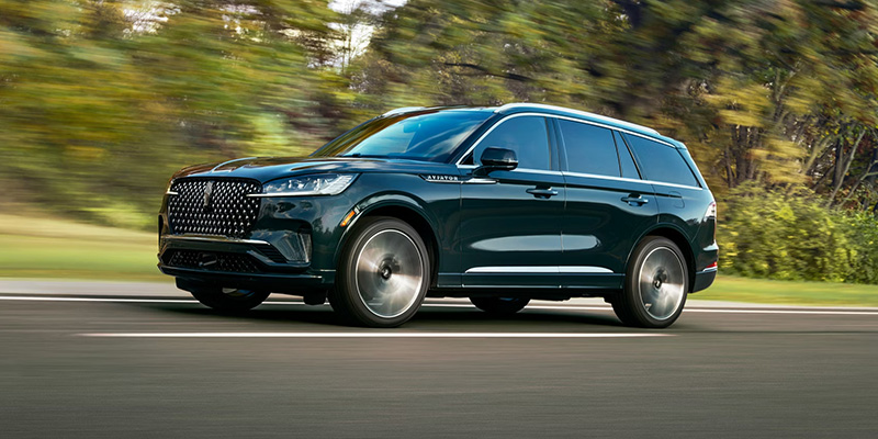 Dark blue Lincoln SUV driving on a road with motion blur and trees in the background.