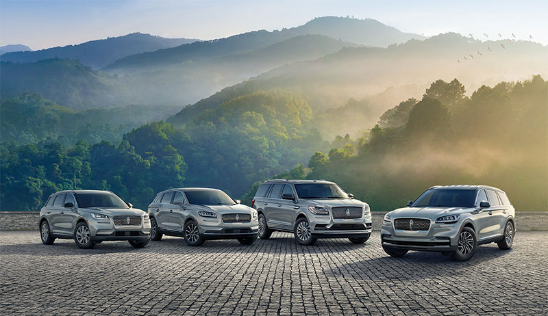 Four silver Lincoln SUVs lined up on a paved surface with misty mountains in the background.
