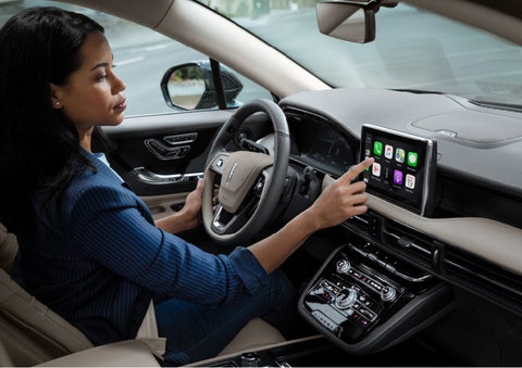 A woman in the driver's seat of a 2022 Lincoln Corsair is touching the center digital screen to connect to Apple CarPlay® | Bob Maxey Lincoln in Detroit MI