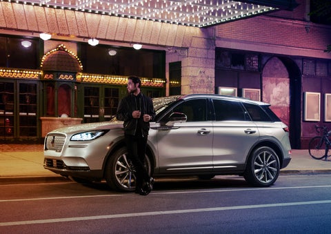 A 2022 Lincoln Corsair SUV is parked outside a theater as the driver relaxes against the frame and lights illuminate the floating roofline and body | Bob Maxey Lincoln in Detroit MI