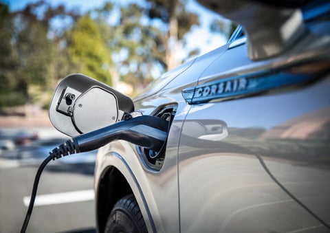 A Lincoln electric charger is plugged into a 2022 Lincoln Corsair Grand Touring port as the body reflects the surroundings of a sun-soaked parking lot | Bob Maxey Lincoln in Detroit MI