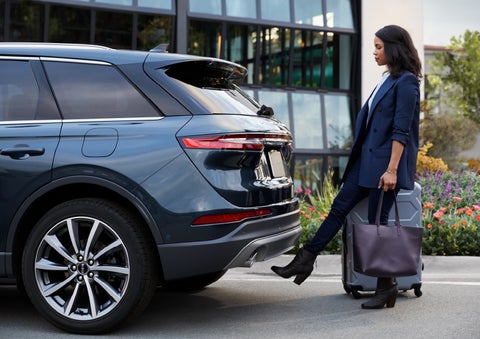 A woman with luggage and a bag opens the available hands-free liftgate by kicking her foot under the bumper | Bob Maxey Lincoln in Detroit MI