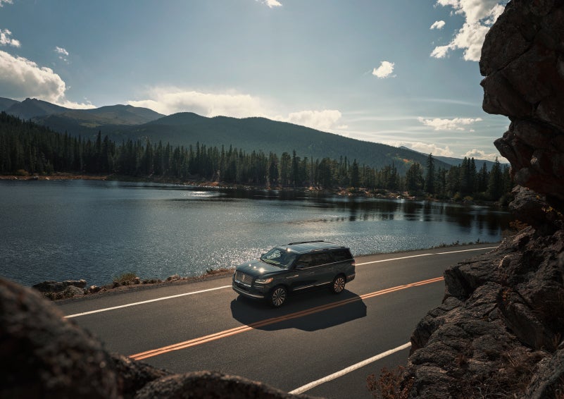 A 2022 Lincoln Navigator SUV is driving along a lake high up in the mountains | Bob Maxey Lincoln in Detroit MI