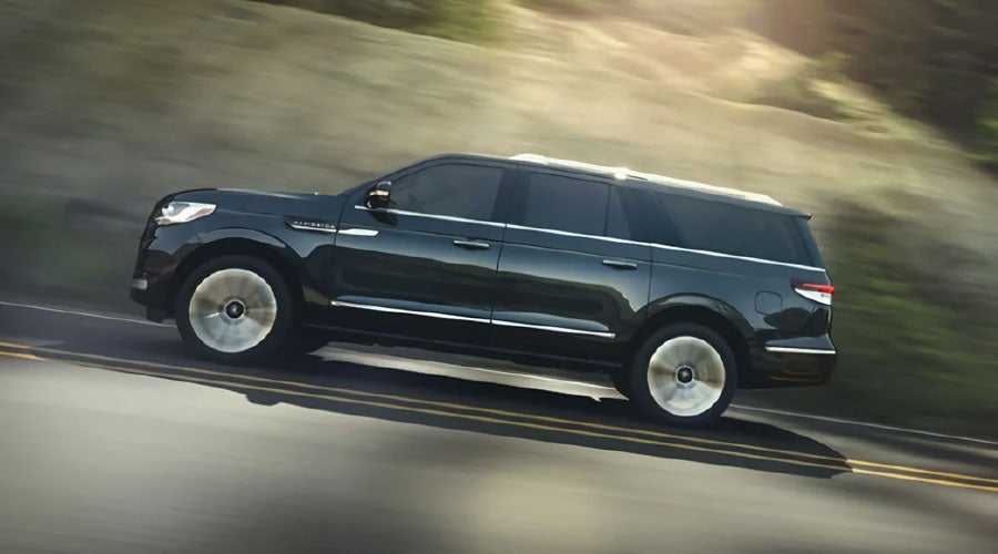 A 2022 Lincoln Navigator is being driven on a freeway bathed in sunlight