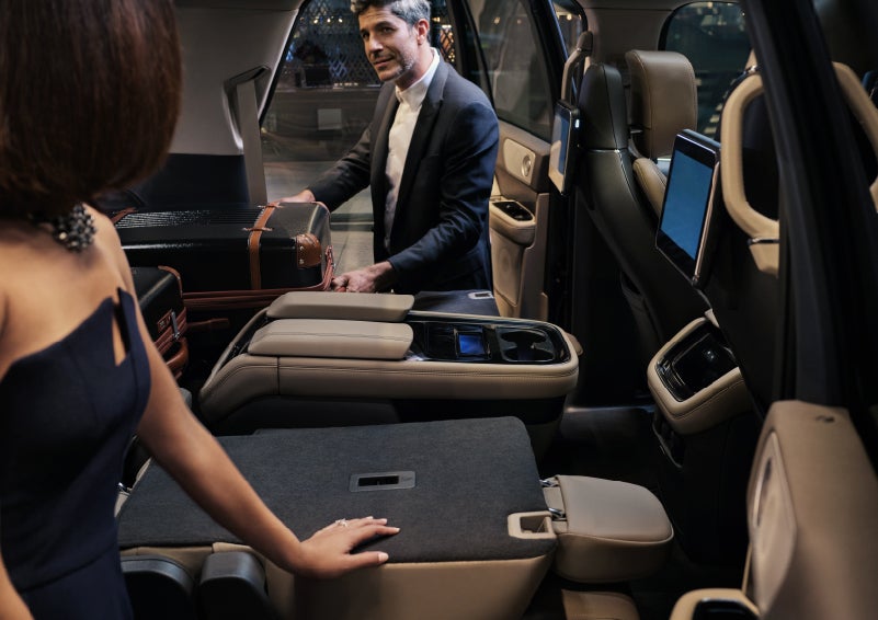 A man is pulling a suitcase out of the folded flat second-row of a 2022 Lincoln Navigator SUV | Bob Maxey Lincoln in Detroit MI