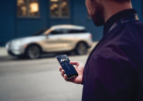 A person is shown interacting with a smartphone to connect to a Lincoln vehicle across the street. | Bob Maxey Lincoln in Detroit MI