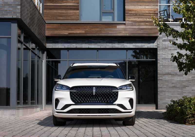A white 2025 Lincoln Aviator® SUV is shown parked outside a modern building with gray brick and wood accents. | Bob Maxey Lincoln in Detroit MI