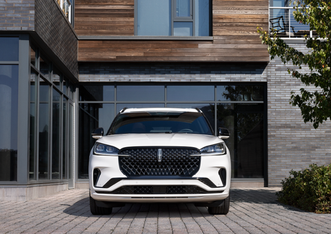 A white 2025 Lincoln Aviator® SUV is shown parked outside a modern building with gray brick and wood accents. | Bob Maxey Lincoln in Detroit MI