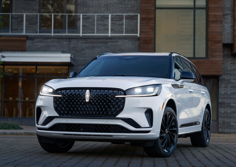 A white 2025 Lincoln Aviator® SUV is shown parked outside a modern building with gray brick and wood accents. | Bob Maxey Lincoln in Detroit MI