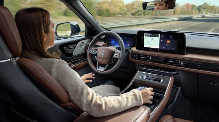 A 2027 Lincoln Aviator® SUV is being driven hands-free on a highway lined with trees. | Bob Maxey Lincoln in Detroit MI