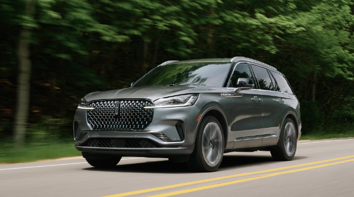 A 2027 Lincoln Aviator® SUV is being driven down a road lined with trees. | Bob Maxey Lincoln in Detroit MI